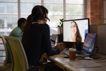 Visão traseira de empresária fazendo videochamada para parceiro de negócios no escritório na mesa — Fotografia de Stock