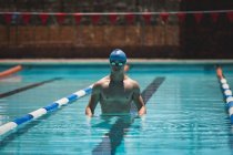 Vista frontal do jovem nadador caucasiano em pé na piscina exterior no dia ensolarado — Fotografia de Stock