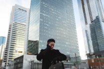 Vue à angle bas de jeune homme d'affaires asiatique regardant smartwatch tout en parlant sur téléphone mobile dans la rue dans la ville — Photo de stock