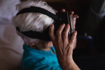 Высокий угол обзора активной пожилой женщины-инвалида, использующей гарнитуру виртуальной реальности, сидя дома на инвалидной коляске — стоковое фото