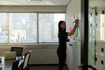 Seitenansicht einer jungen hübschen weiblichen Führungskraft, die auf bunten Zetteln in einem modernen Büro schreibt — Stockfoto