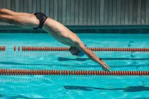 Vista laterale del giovane nuotatore caucasico che si tuffa nell'acqua di una piscina all'aperto nella giornata di sole — Foto stock