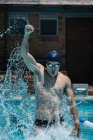 Vista frontal do jovem nadador masculino caucasiano comemora a vitória e levanta o punho na piscina ao ar livre ao sol — Fotografia de Stock