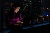 Vista frontal de muito jovem mestiço executivo feminino trabalhando no laptop perto da janela em um escritório moderno — Fotografia de Stock