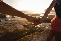 Close up of African-american couple holding hands and standing on rock near sea side — Stock Photo