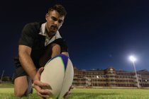 Vista de ángulo bajo del jugador de rugby que coloca la pelota de rugby en la camiseta de patadas en el estadio por la noche - foto de stock