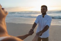 Вид сбоку молодой влюбленной пары, держащейся за руку, стоя на пляже в солнечный день. Они наслаждаются отпуском. — стоковое фото