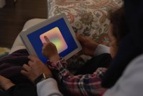 Високий кут зору змішаної раси мати і дочка, використовуючи цифровий планшет вдома на дивані у вітальні — стокове фото