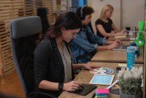 Seitenansicht einer kaukasischen Geschäftsfrau, die ein Grafik-Tablet benutzt, während sie im Büro Farbmuster betrachtet, während Kollegen hinter ihr arbeiten — Stockfoto