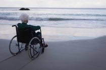 Задній вид відключені жінка активних старшим дивлячись на море, сидячи на кріслі-візку на пляжі — стокове фото