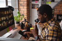 Vista lateral do empresário afro-americano pensativo trabalhando no computador segurando o telefone celular no escritório — Fotografia de Stock