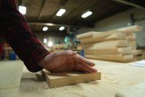 Primer plano del carpintero trabajando en el taller. Su mano se coloca en una tabla de madera - foto de stock