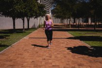 Вид спереду на активну старшу жінку, яка бігає в парку в сонячний день — стокове фото