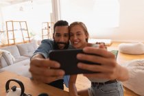 Vista frontale della coppia etnica che si fa selfie in soggiorno a casa — Foto stock