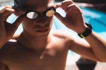 Close-up do jovem nadador masculino caucasiano ajustando óculos de natação enquanto usava relógio na piscina exterior no dia ensolarado — Fotografia de Stock