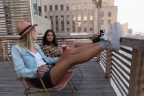 Seitenansicht multiethnischer Freundinnen, die bei einem kühlen Getränk auf dem Balkon miteinander reden — Stockfoto