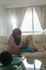 Vue de face de la mère métisse portant le hijab à sa fille dans le salon à la maison — Photo de stock