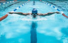 Vue de face du jeune nageur masculin caucasien nageant course de papillon dans la piscine extérieure par une journée ensoleillée — Photo de stock
