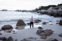 Rückansicht einer aktiven Seniorin, die am Ufer des Strandes spaziert — Stockfoto