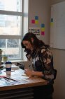 Вид збоку кавказької бізнес-леді, що сидить і пише в блокноті в офісі — стокове фото