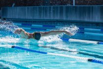 Vue de face d'un nageur mâle nageant en style libre papillon dans la piscine par une journée ensoleillée — Photo de stock