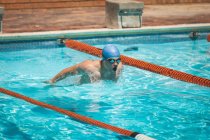 Vista frontal de un joven nadador masculino caucásico nadando mariposa en una piscina al aire libre en un día soleado - foto de stock
