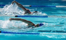 Vue latérale du jeune nageur mâle et femelle rampant côte à côte dans la piscine par une journée ensoleillée — Photo de stock