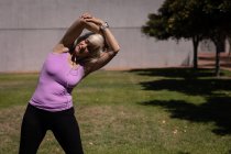 Vista frontal de uma mulher idosa ativa se exercitando e se alongando no parque em um dia ensolarado — Fotografia de Stock