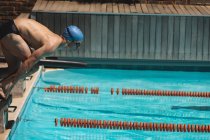 Vista laterale del giovane nuotatore maschio caucasico che salta nell'acqua di una piscina all'aperto sotto il sole — Foto stock