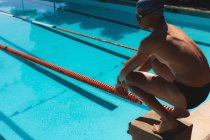 Вид збоку молодих кавказьких чоловіків плавець crouching на стартову блоку на відкритий плавальний басейн на сонячний день — стокове фото