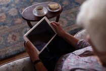 Високий кут зору активної старшої жінки, використовуючи цифровий планшет, сидячи на дивані вдома для сонечка — стокове фото