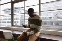 Vue de face de l'homme d'affaires afro-américain utilisant un téléphone portable alors qu'il est assis sur la table dans la cantine de bureau — Photo de stock