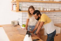 Side view of multi ethnic Couple standing and working over laptop at home in kitchen room — Stock Photo