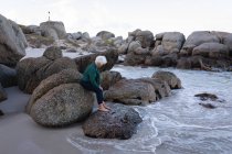 Vista laterale di una donna anziana attiva seduta sugli scogli in spiaggia — Foto stock