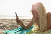 Seitenansicht einer blonden Frau, die an einem sonnigen Tag ein Selfie am Strand macht — Stockfoto