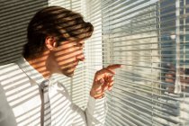 Side view of handsome young male executive looking through window blinds in a modern office — Stock Photo