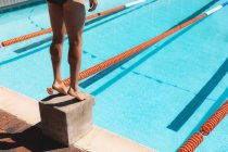 Low section of male swimmer standing starting block at outdoor swimming pool in the sunshine — Stock Photo