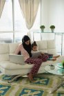 Frontansicht einer Mutter mit Hijab, die mit ihrer Tochter spricht, während sie ihr digitales Tablet im heimischen Wohnzimmer zeigt — Stockfoto