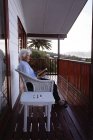 Seitenansicht einer aktiven Seniorin, die ein Buch liest, während sie zu Hause auf einem Sessel auf dem Balkon sitzt — Stockfoto