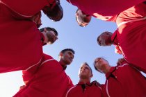 Vista de bajo ángulo de jugadores de rugby multiétnicos masculinos formando grupos e interactuando en el campo de rugby - foto de stock