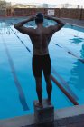 Vista posteriore di un nuotatore caucasico maschio che indossa il suo occhiale da nuoto mentre si trova su un blocco di partenza e guarda la piscina — Foto stock
