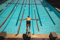 Высокий угол обзора молодого кавказского пловца с вытянутыми руками, прыгающего в воду бассейна в солнечный день — стоковое фото