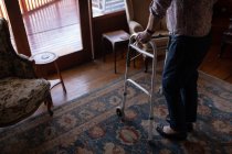 Низкая часть активной пожилой женщины, идущей с ходунком в гостиной дома — стоковое фото