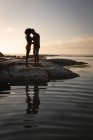 Vista frontal do casal afro-americano de pé em humor romântico perto do lado do mar na rocha — Fotografia de Stock