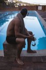 Vista lateral de um nadador caucasiano sentado no bloco de partida perto da piscina — Fotografia de Stock