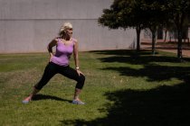 Вид спереду на активну старшу жінку, яка займається спортом і розтягується в парку в сонячний день — стокове фото