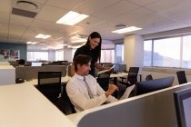 Vista frontal de jóvenes ejecutivos trabajando y discutiendo sobre documentos en el escritorio en una oficina moderna - foto de stock