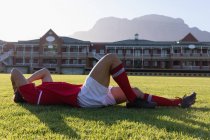 Vista lateral de um jogador de rugby caucasiano machucado deitado no chão ao sol — Fotografia de Stock