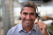 Porträt eines glücklichen Geschäftsmannes, der in die Kamera lächelt, während er einen Kopfhörer im Büro hält — Stockfoto