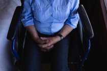 Средний вид на инвалида пожилой женщины со сцепленными руками, сидящей на инвалидном кресле в спальне дома — стоковое фото